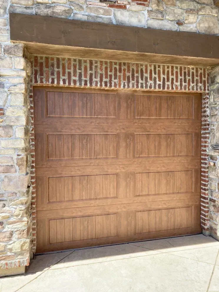 Wooden garage door set in a stone wall with brick trim above, viewed from outside