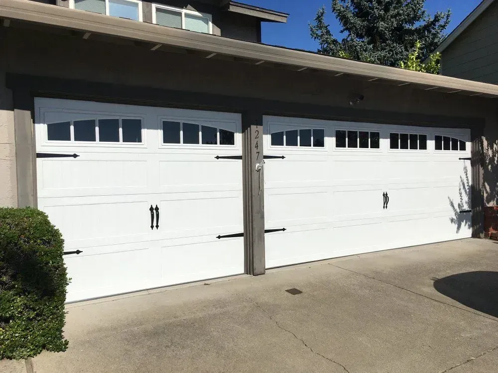 Two white garage doors with small windows on a suburban house driveway