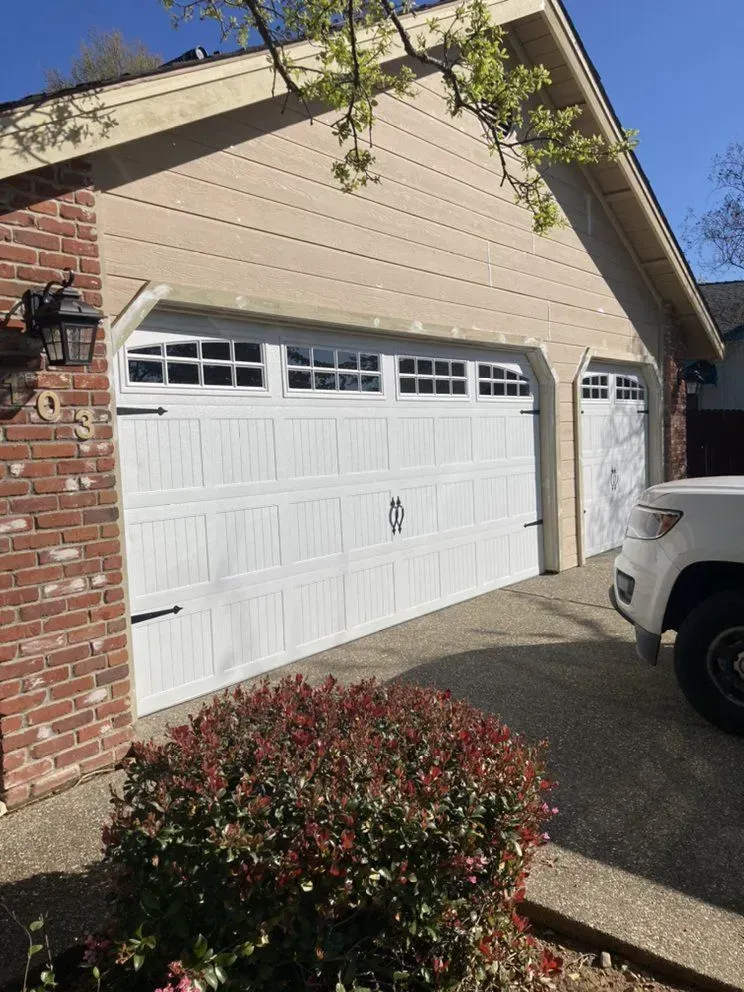 Suburban house exterior with a white garage door, beige siding, brick wall, and parked white vehicle beside driveway
