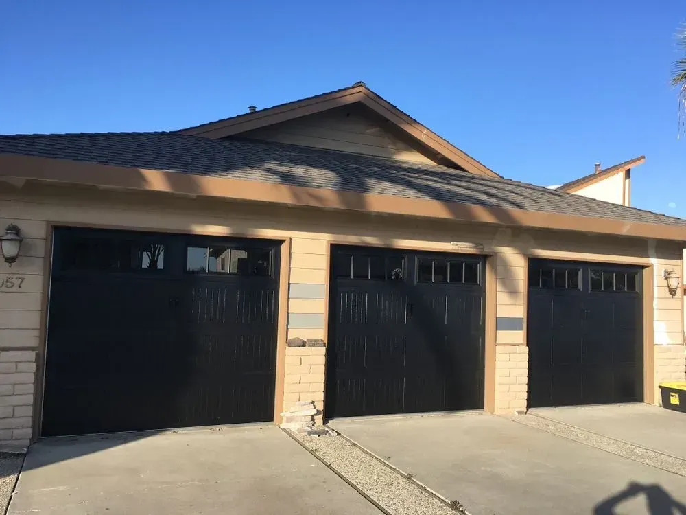 Three-car garage with beige stucco exterior, black doors, and a blue sky overhead