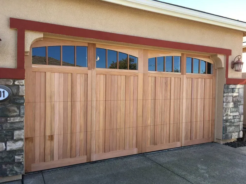Wooden double garage door with arched window panes on a stone-and-stucco house exterior