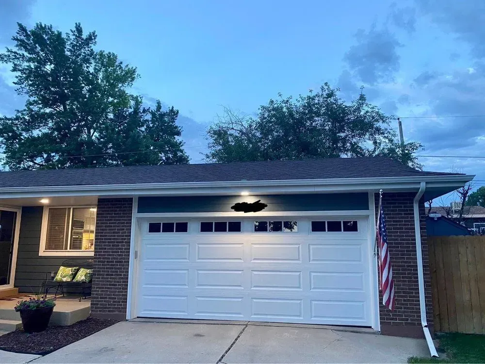 Single-story brick house at dusk with a white garage door and an American flag by the entrance