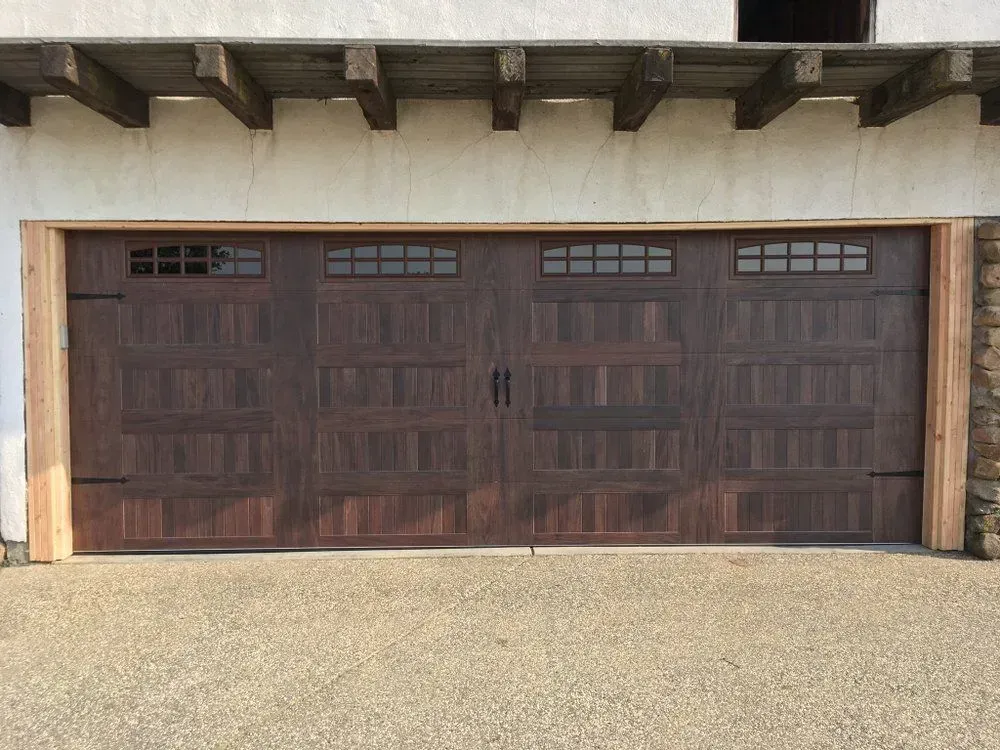 Wide dark brown wooden garage door with small windows in a stucco driveway opening