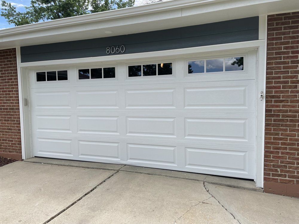 A white garage door is sitting in front of a brick building.
