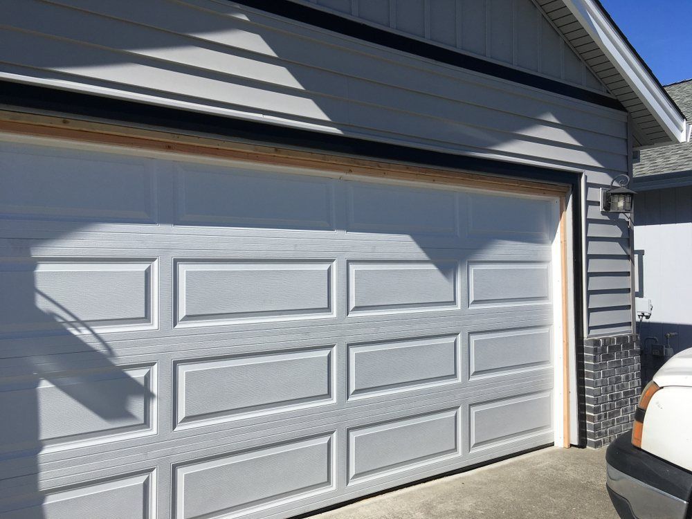 A white car is parked in front of a white garage door.
