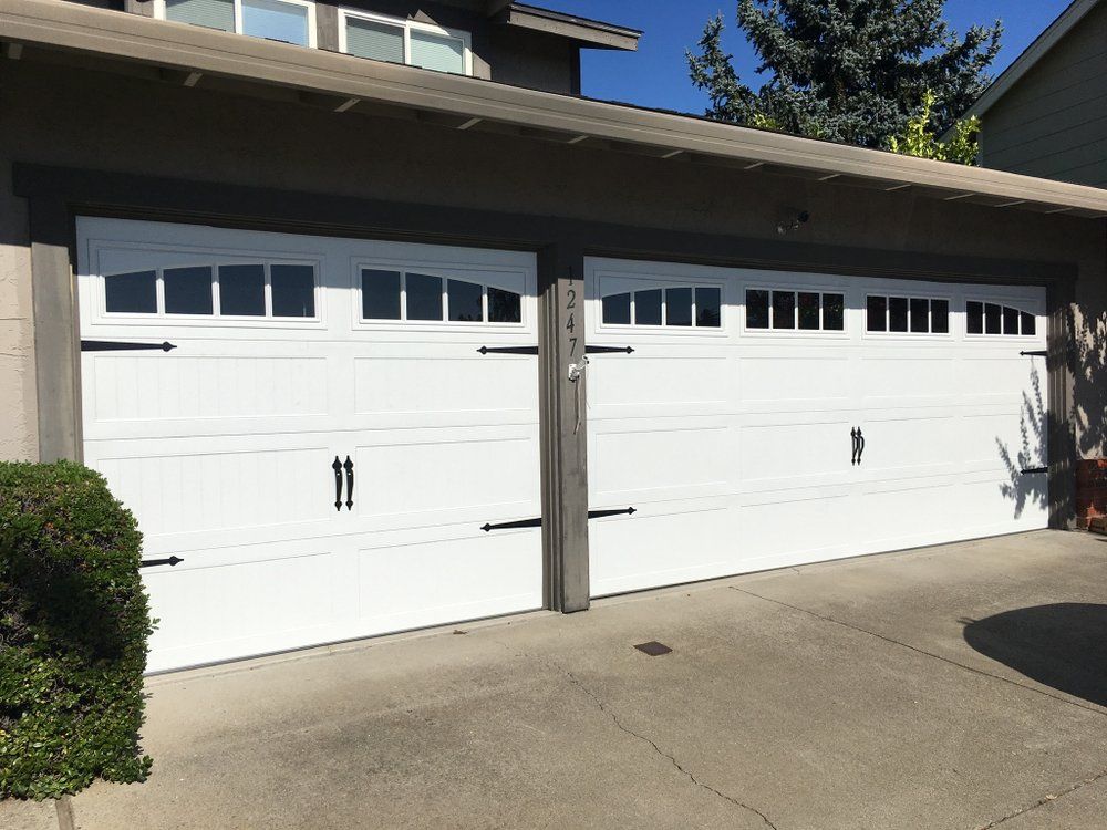 Two white garage doors are sitting next to each other in front of a house.