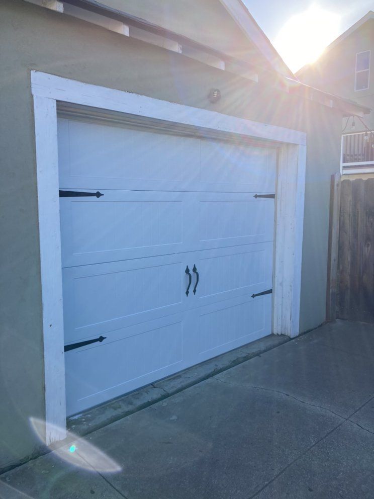A white garage door with black handles is sitting on a sidewalk next to a house.
