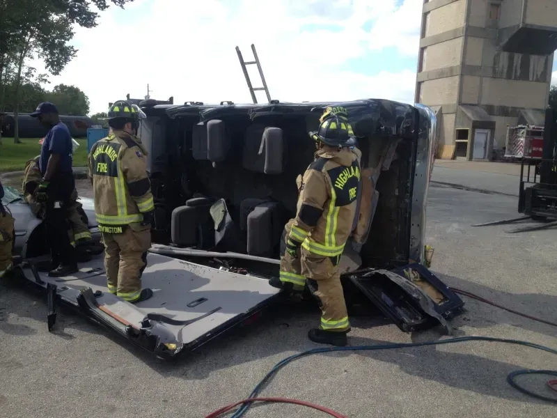A group of firefighters are working on a car that has been flipped over
