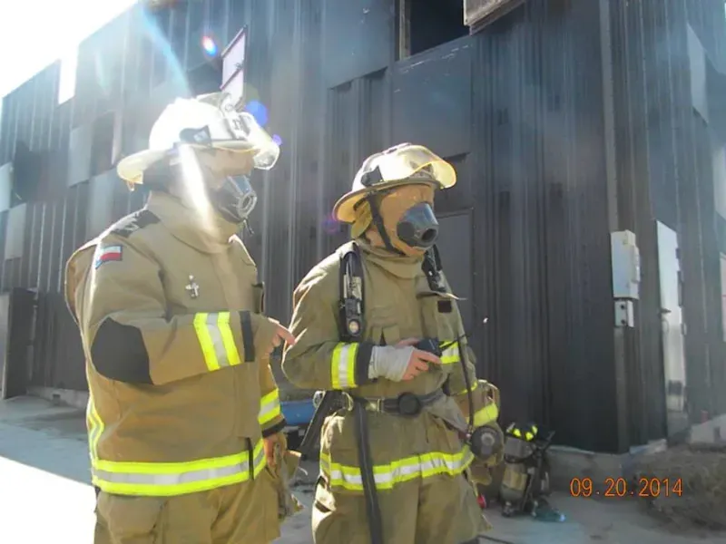 Two firefighters are standing next to each other in front of a training building.