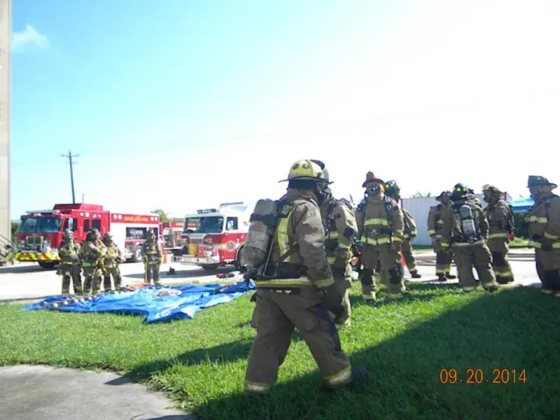a large group of  firefighters standing in front of a fire truck during a training exercise.