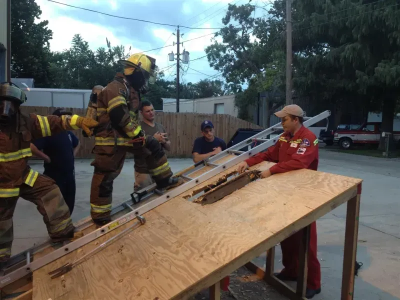 A group of firefighters are standing around a wooden table.