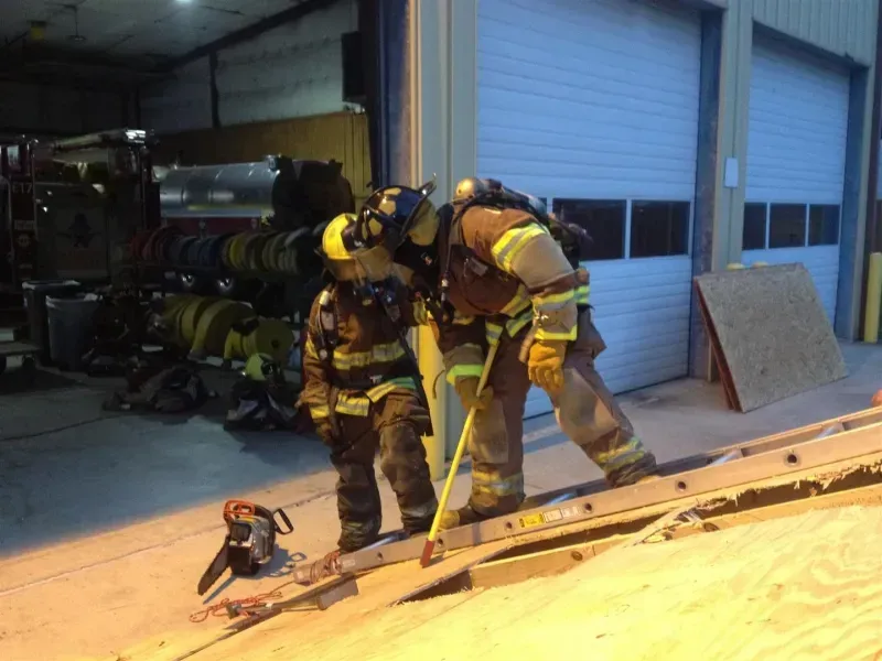 Two firefighters are measuring a ladder in a garage.