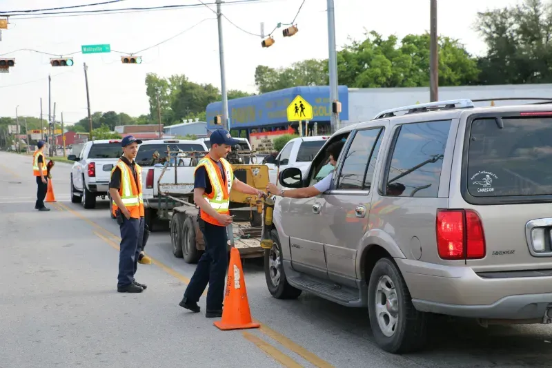 A man in a safety vest is talking to a man in a car.