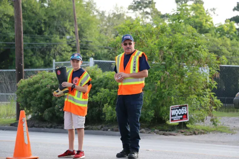 A man and a boy are standing next to each other on the side of the road holding fire boots for MDA fill the boot.