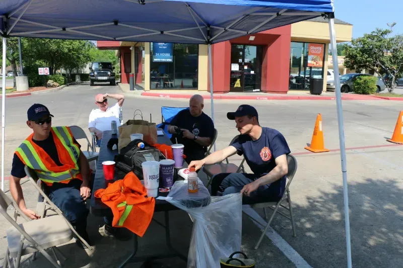 A group of firefighters are sitting under a tent in a parking lot