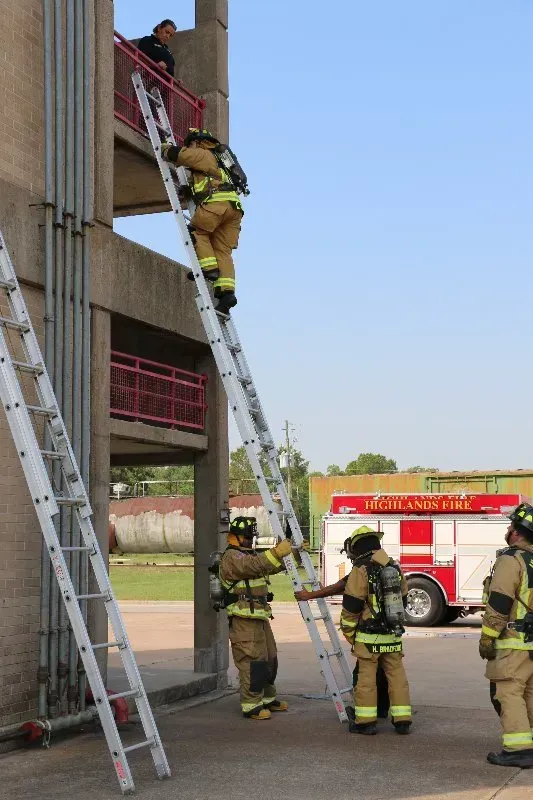 A group of firefighters are climbing ladders in front of a fire truck.