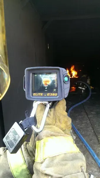 A fireman is holding a thermal camera in front of a fire.