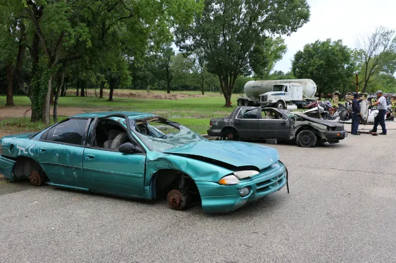 A green car with a broken windshield is parked next to a black car.