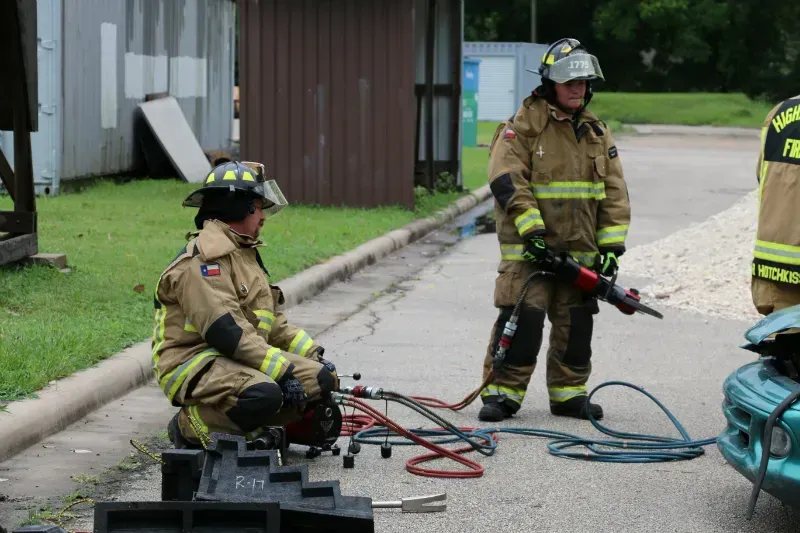 A group of firefighters are working on a car on the side of the road.
