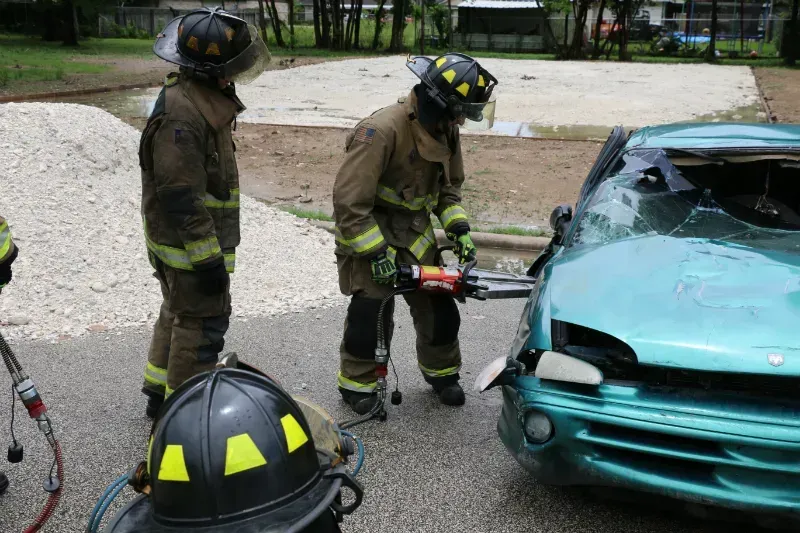 Two firefighters are working on a green car