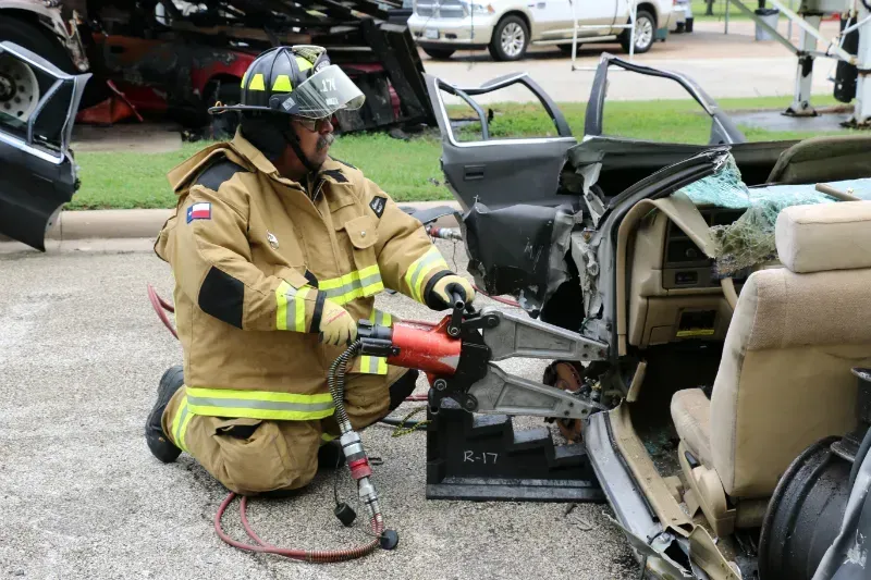 A fireman is kneeling down next to a damaged car