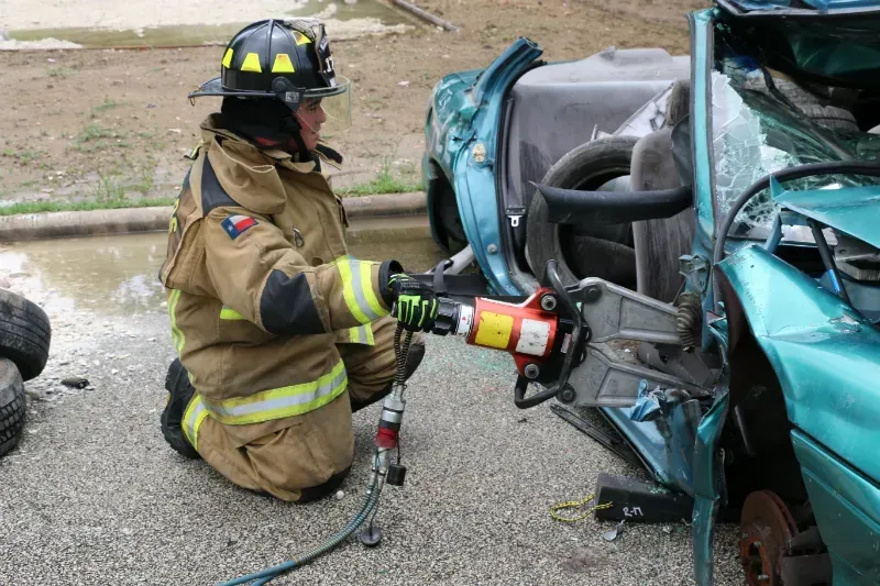 A fireman is kneeling down next to a damaged car.