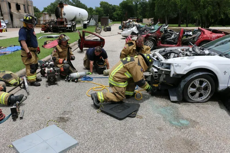 A group of firefighters are working on a car in a parking lot.
