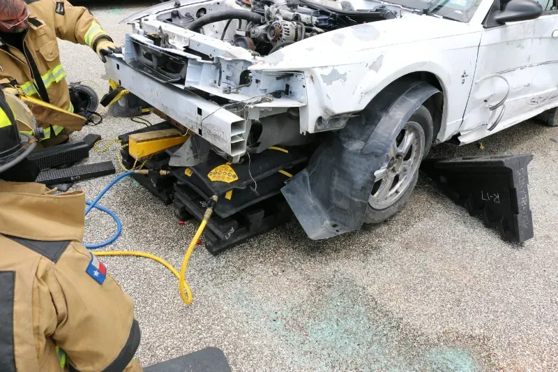 Two firefighters are working on a car that has been damaged in an accident.