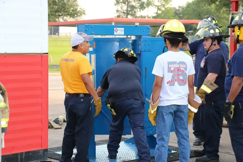 A group of firefighters are standing around a forcible entry training prop.