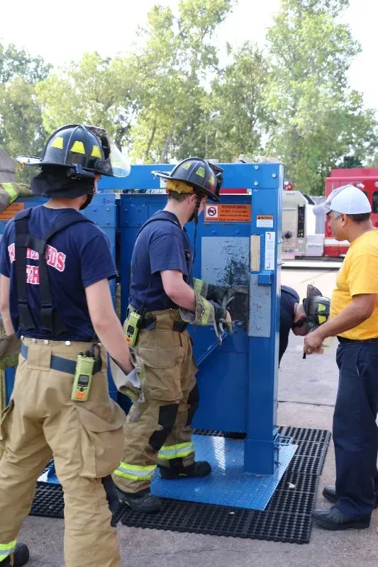 A group of firefighters are standing around a forcible entry training prop.
