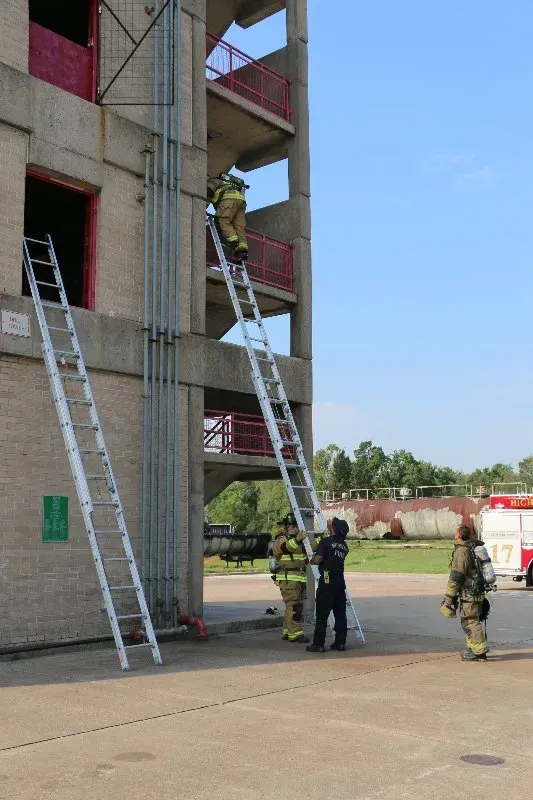 A group of firefighters are climbing ladders in front of a building.