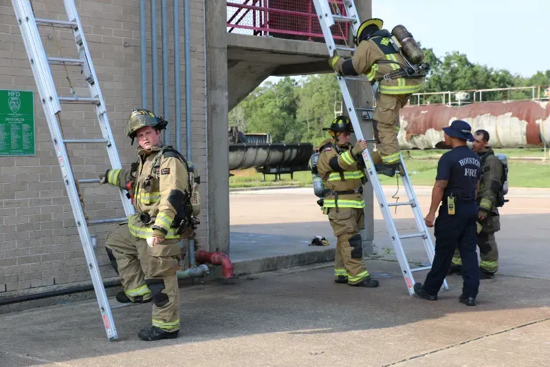 A group of firefighters are standing next to ladders.