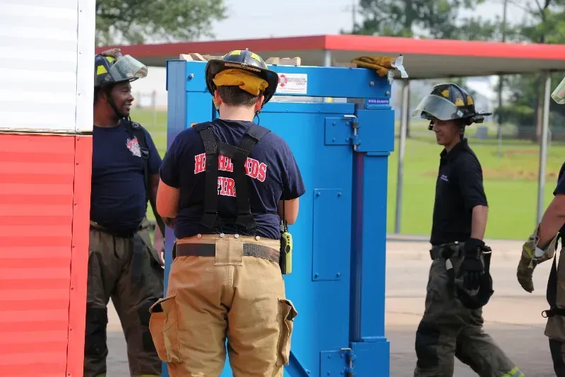 A group of firefighters are standing around a forcible entry training prop.