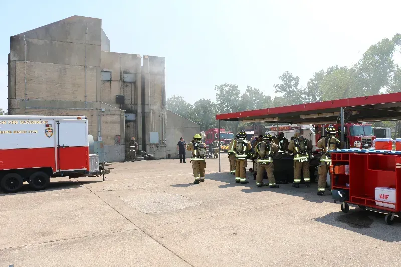 A group of firefighters are standing in a parking lot in front of a training building.