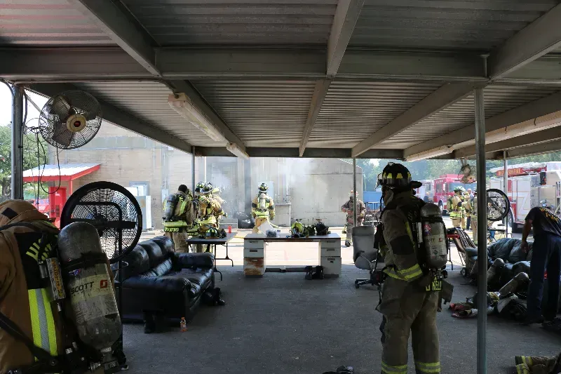 A group of firefighters are resting under a canopy during a training exercise.