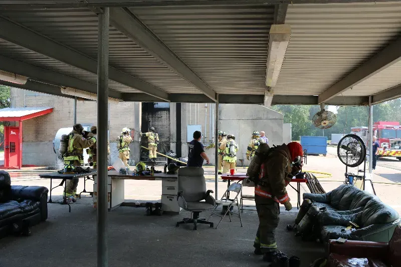 A group of firefighters are resting under a canopy during a training exercise.