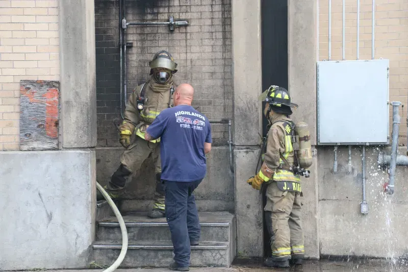 A man in a blue shirt is helping two firefighters with a hose during a training exercise.