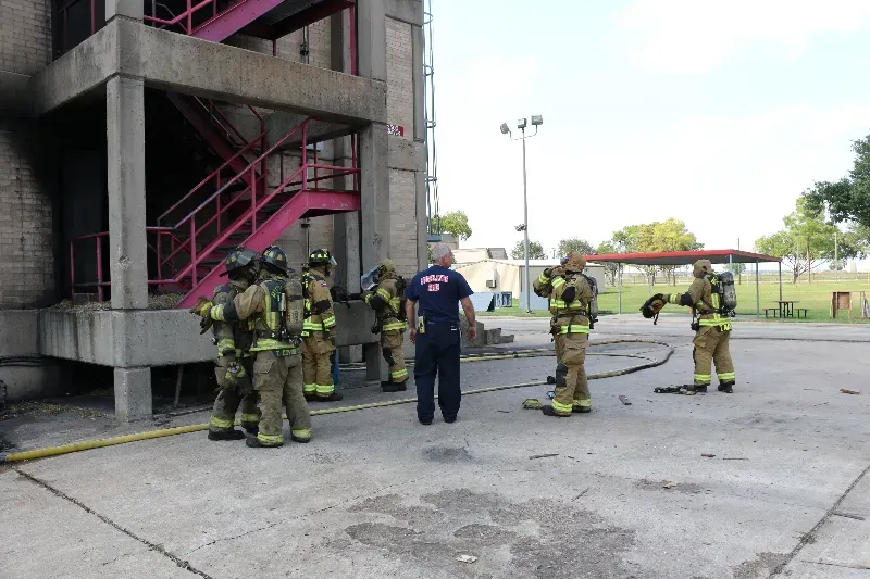 A group of firefighters are standing next to each other next to a training burn building