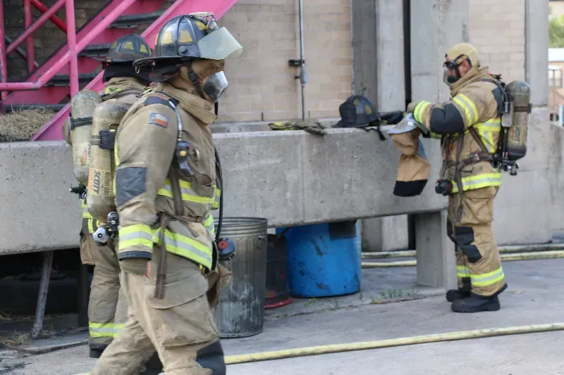 A group of firefighters are standing next to each other next to a training burn building