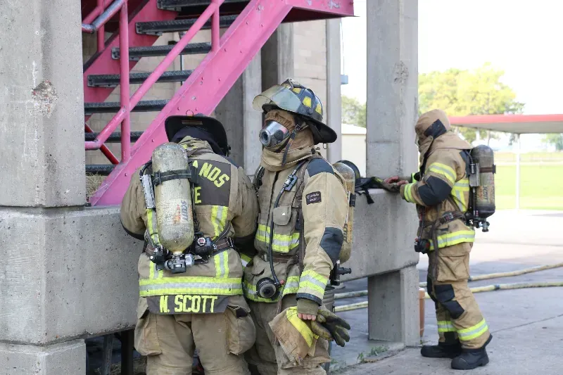 A group of firefighters are standing next to each other next to a training burn building.