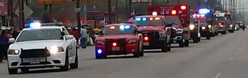 A row of police cars and Highlands Fire Department vehicles are driving down a street during a parade.