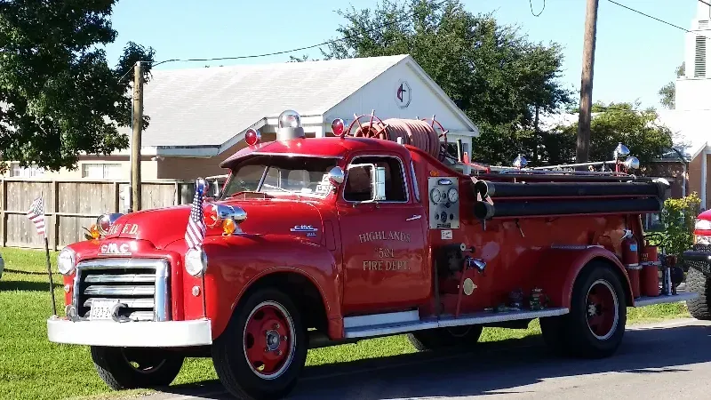 A classic red fire truck is parked on the side of the road getting ready for a parade.