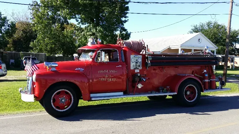 A classic red fire truck is parked on the side of the road getting ready for a parade.
