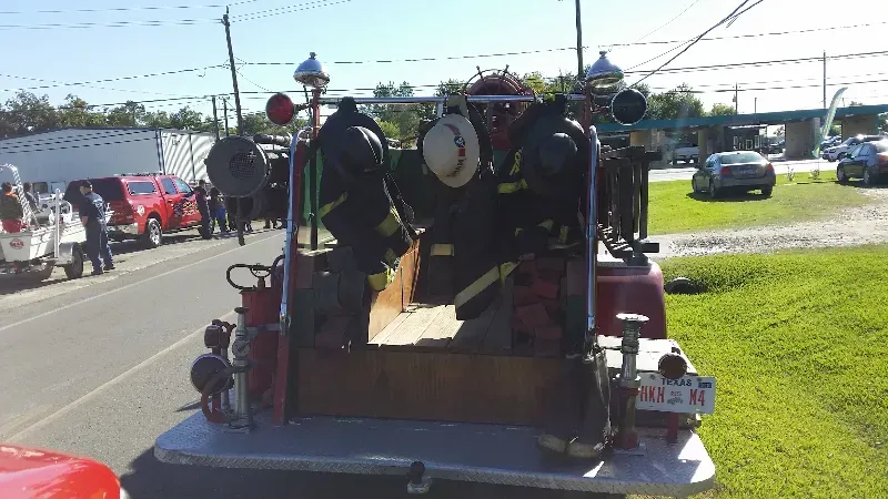 A classic red fire truck is parked on the side of the road getting ready for a parade.