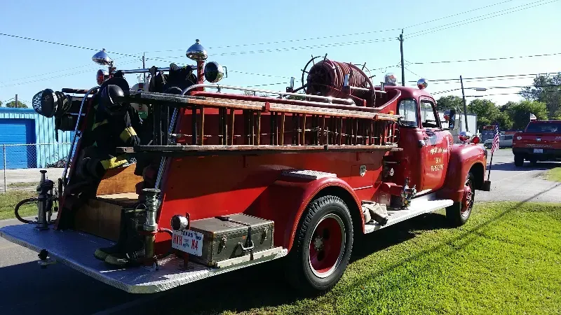 A classic red fire truck is parked on the side of the road getting ready for a parade.