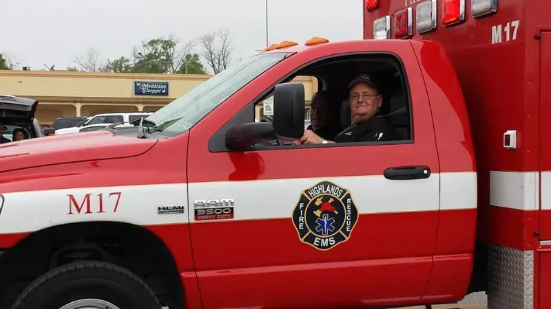 A man is driving an ambulance with the number m17 on the side in a parade.