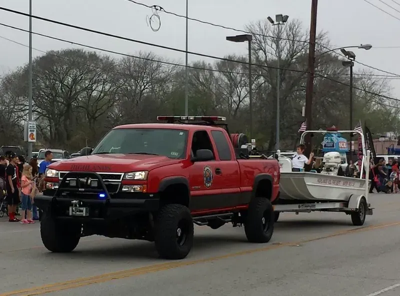 A red fire command vehicle is pulling a boat on a trailer during a parade