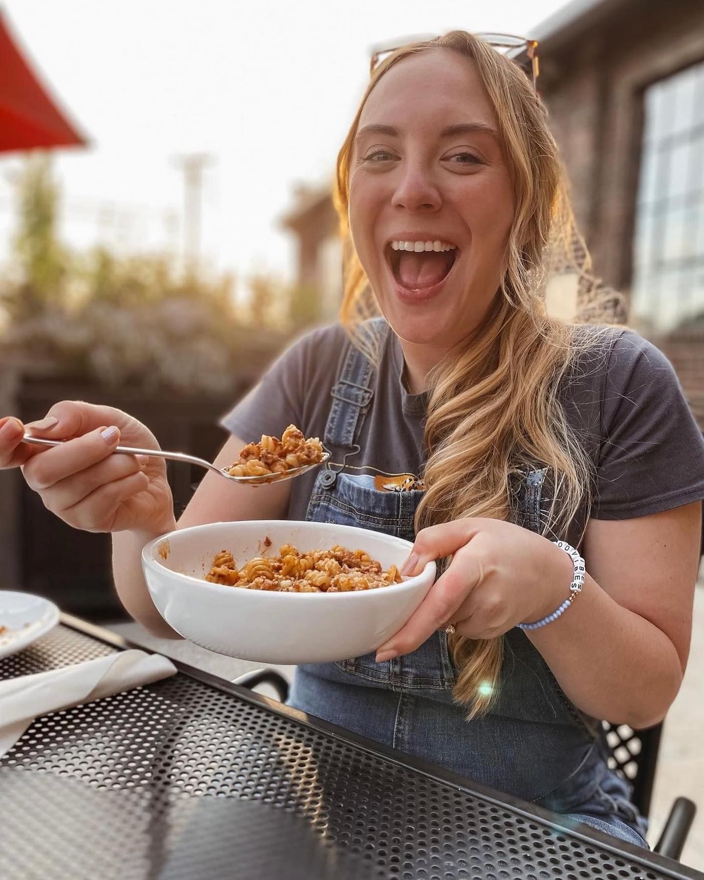 A woman is sitting at a table eating a bowl of food with a spoon.