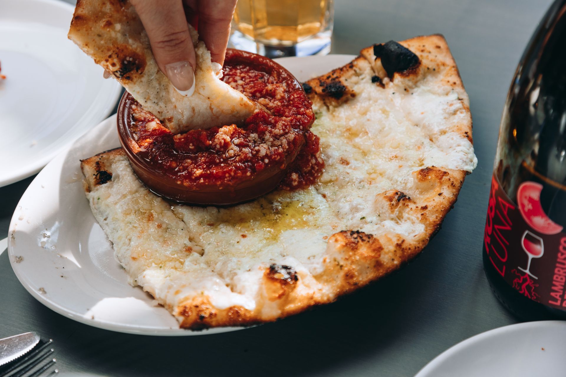A person is dipping a piece of bread into a pizza.
