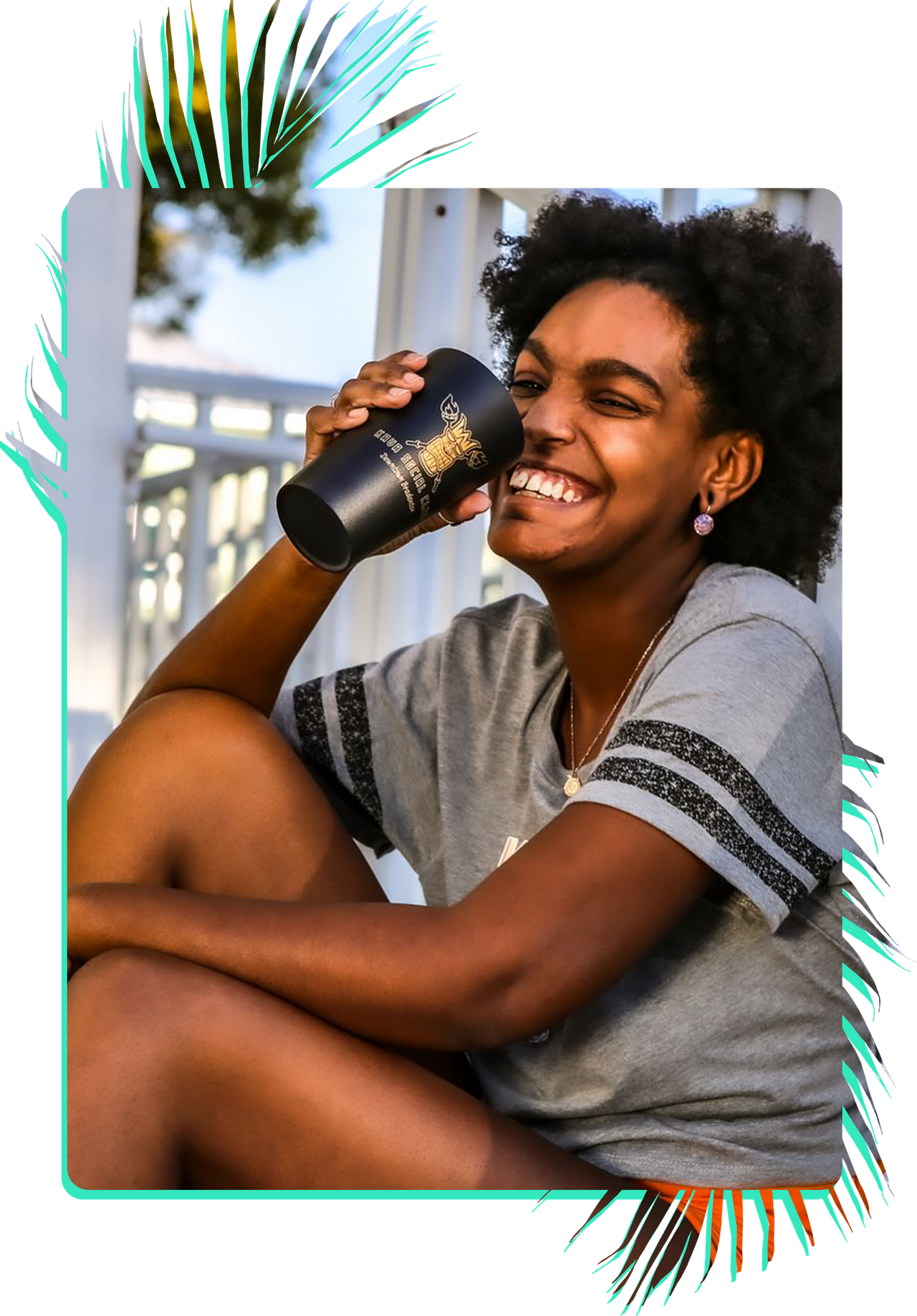 A woman in a pink shirt is holding a black cup and smiling.